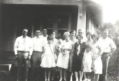 Group of men, women, and children standing together outside of home
