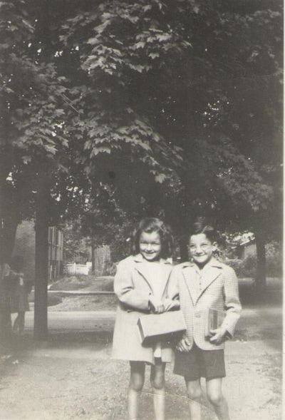 Young boy and girl with books and box standing together on sidewalk