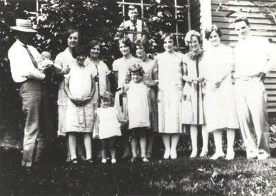Group of men, women, and children standing together behind house