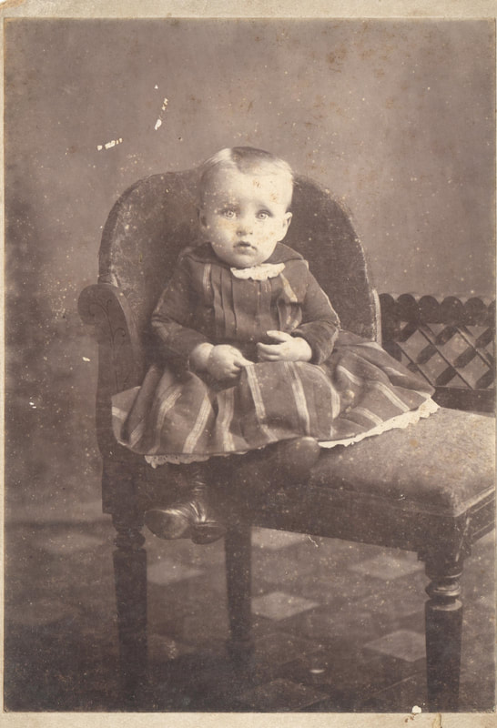 Baby boy in gown seated on chair