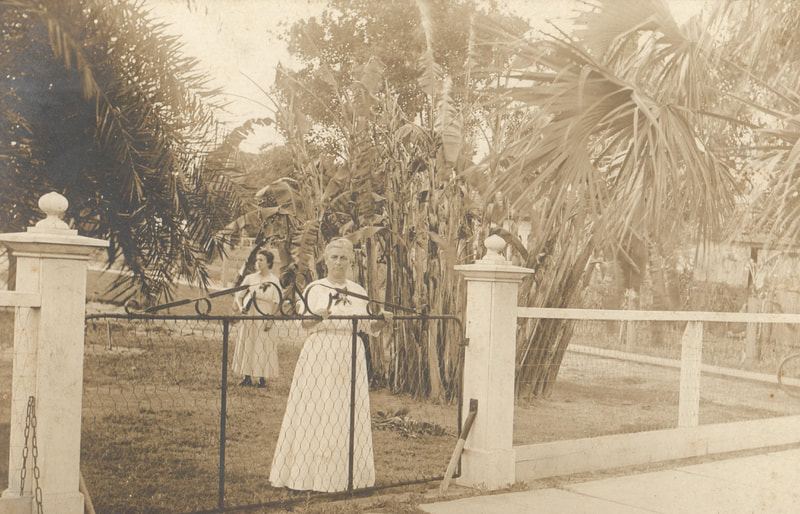 Women in white dresses standing behind fence  