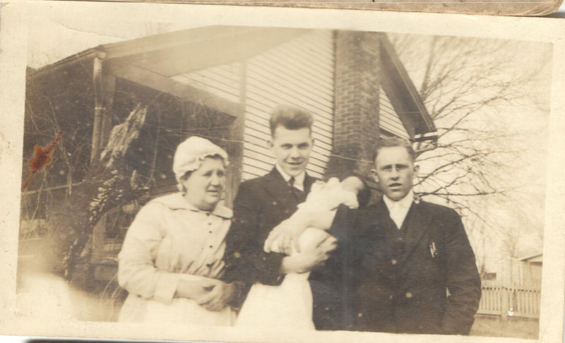 Young man standing holding baby between man and woman in bonnet