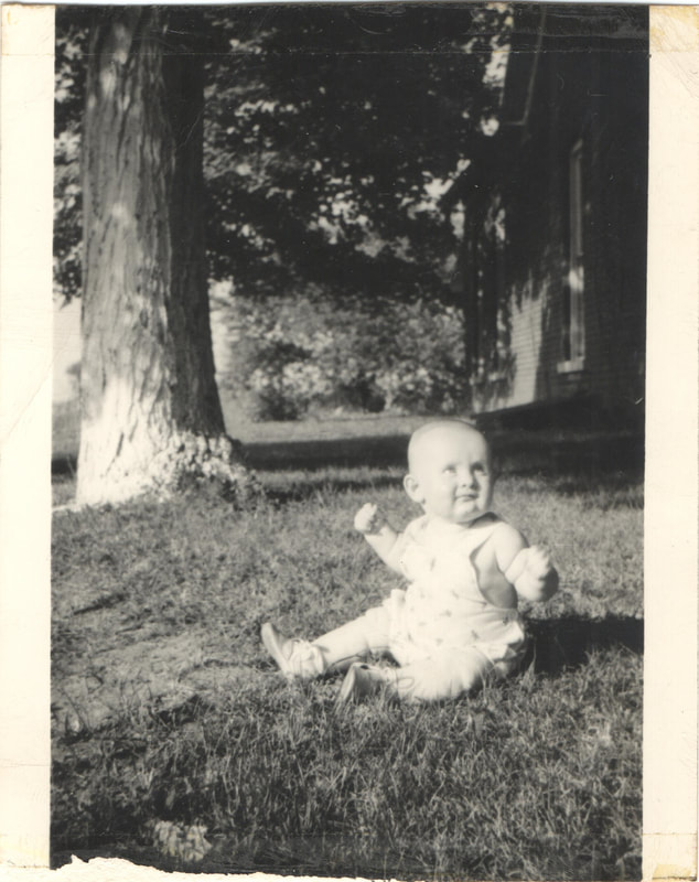 Baby boy with hands in fists sitting on yard