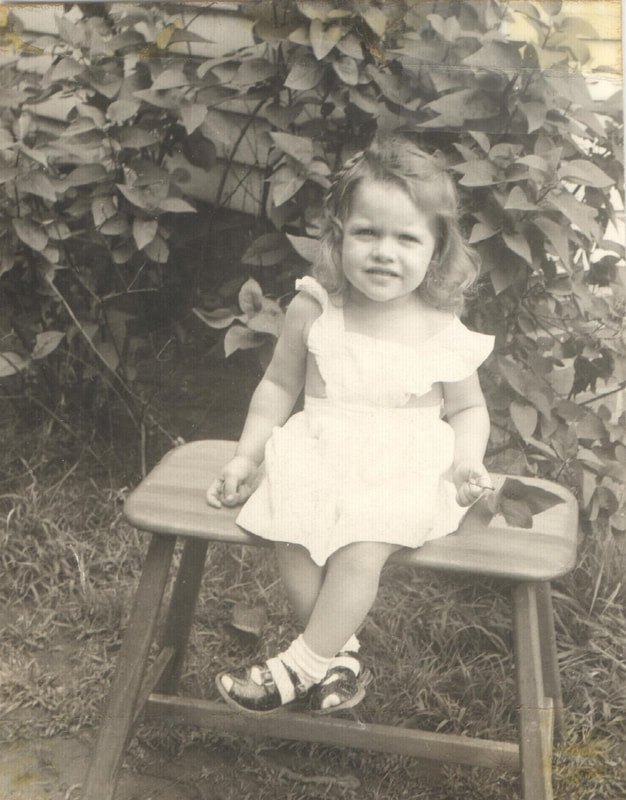 Baby girl with brown hair seated on chair outdoors
