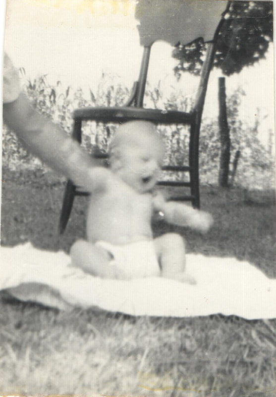 Baby boy in diaper seated on blanket outdoors