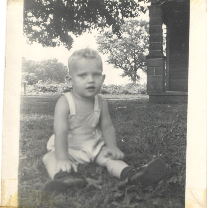 Young boy in overalls sitting on yard