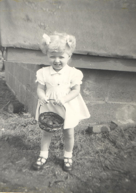 Young girl with blond hair holding basket standing in yard