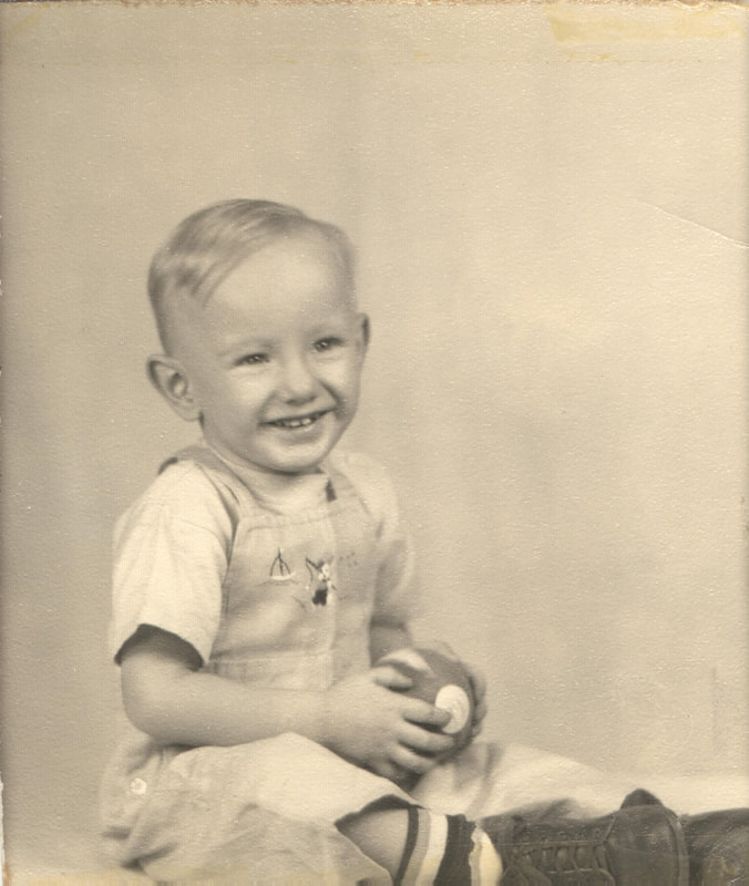 Young boy in overalls holding football seated 