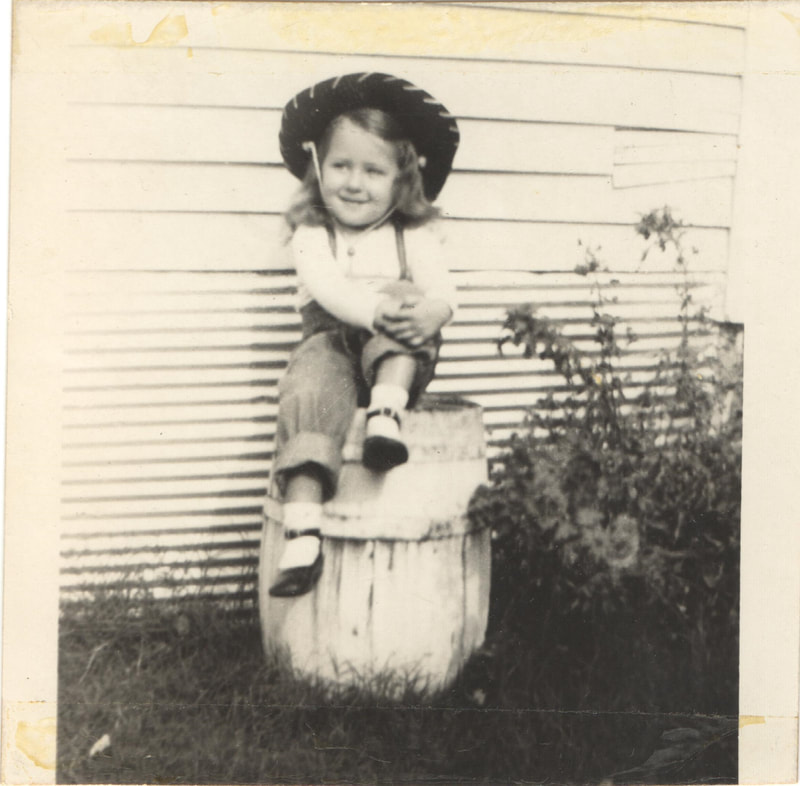 Young girl in hat seated on barrel 