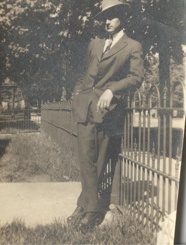 Young man in suit and hat leaning on fence