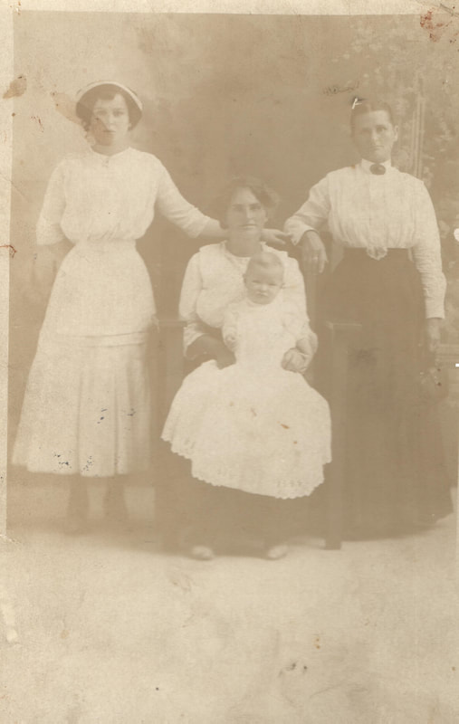 Two women standing beside woman seated with baby