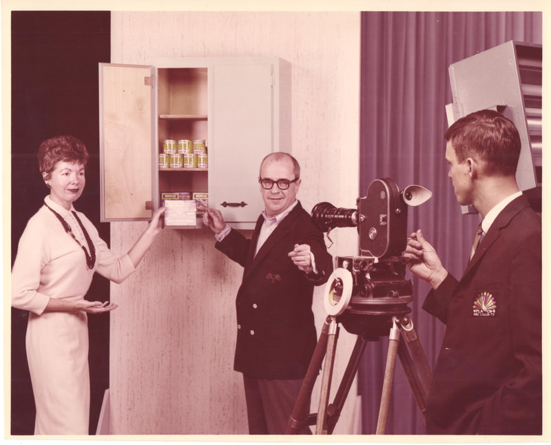 Woman in necklace holding box with man in suit at television shoot