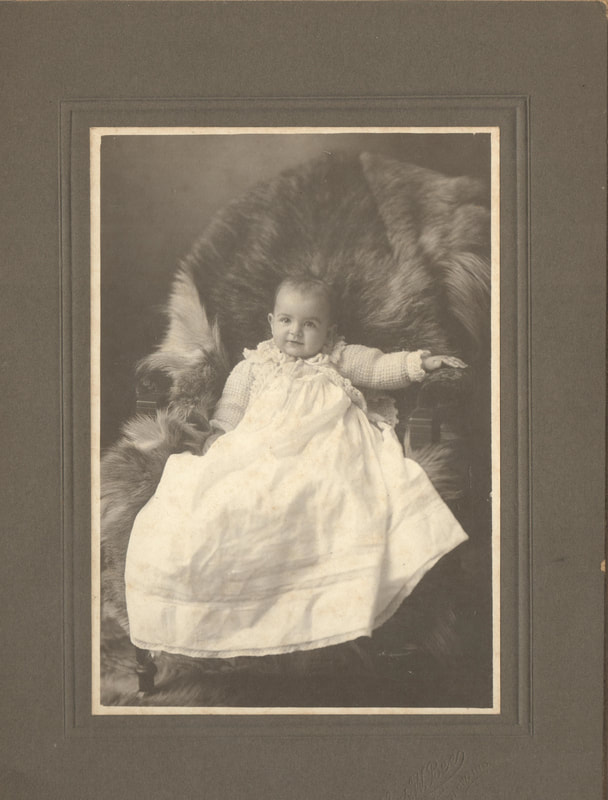 Baby girl in gown seated on chair with fur 