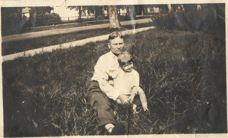 Man and young girl seated together in yard of house