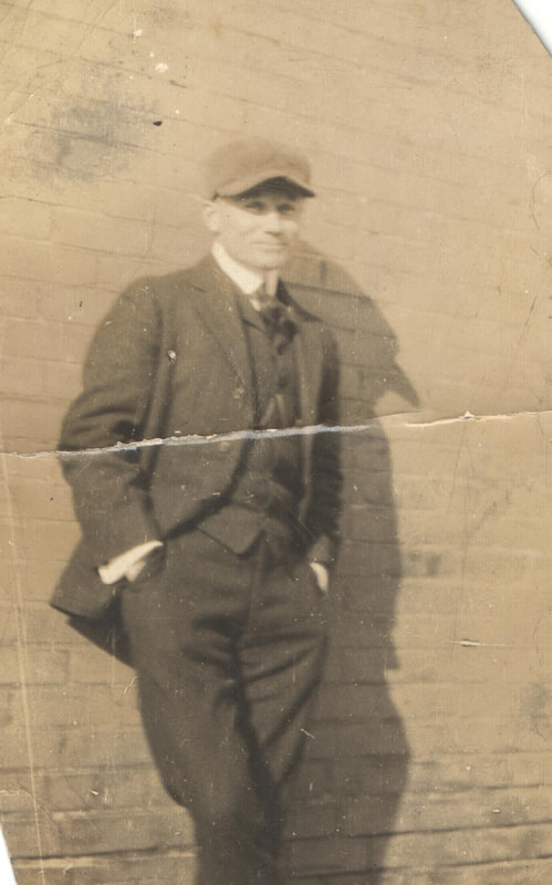 Man in hat and suit leaning against brick building