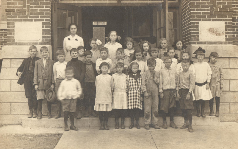 Group of school children and teacher standing in front of school