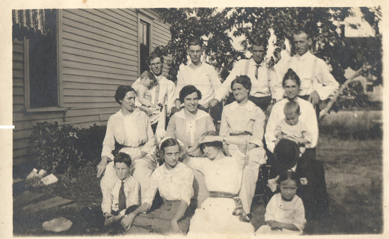 Men standing behind women and child seated near home