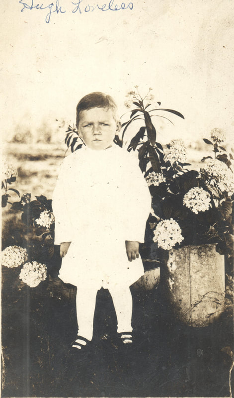 Young boy standing in front of flowers in white gown