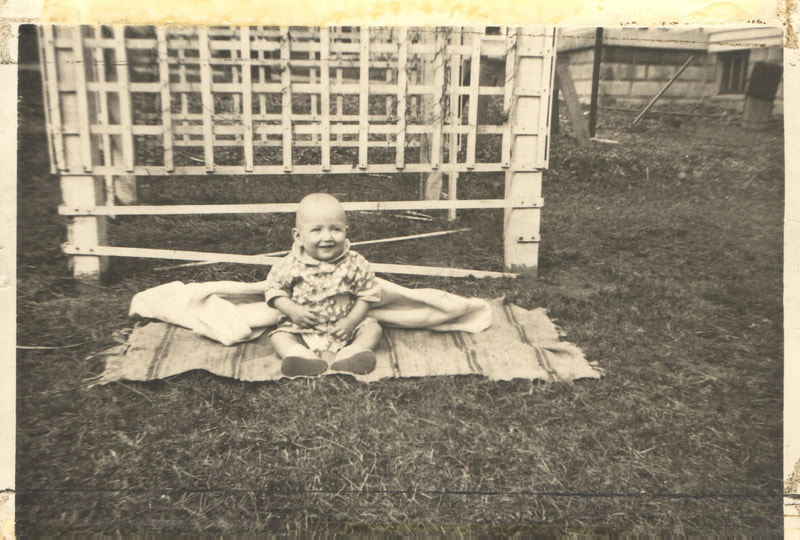 Baby seated on blanket in yard