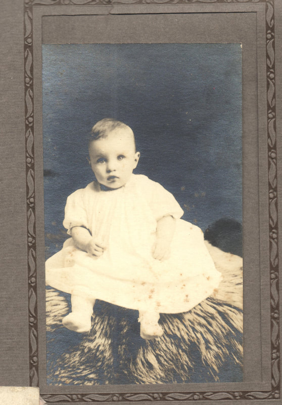 Baby boy in gown seated on fur rug