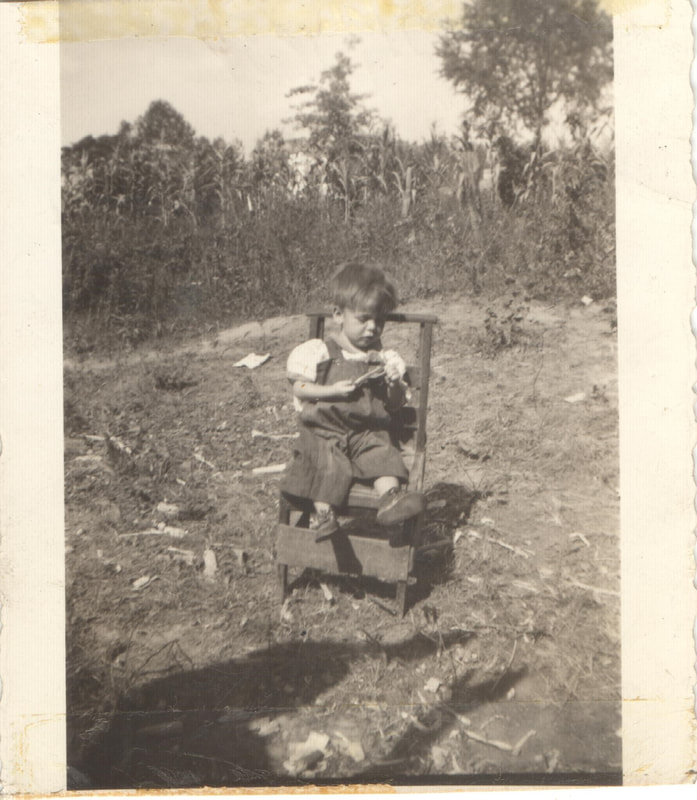 Young boy in overalls seated on chair