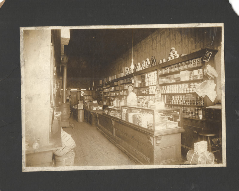 Man standing behind counter of shop, 1900