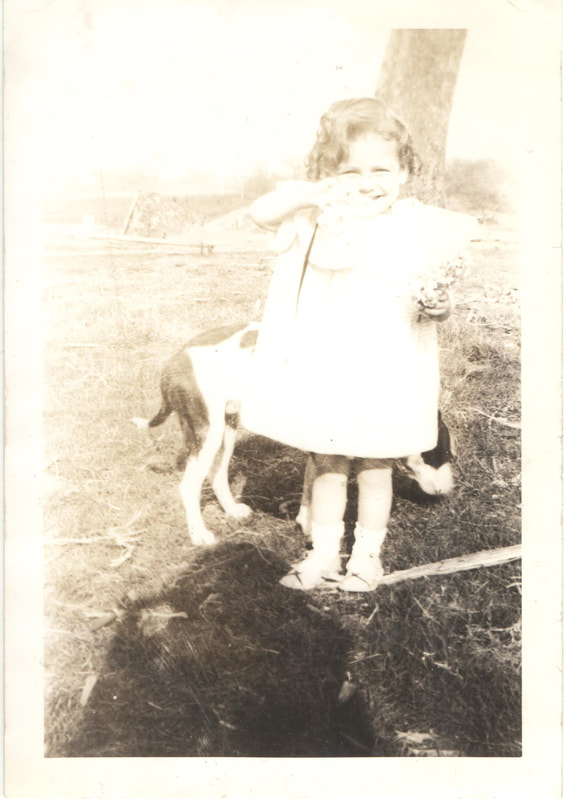 Young girl stands in front of dog in yard