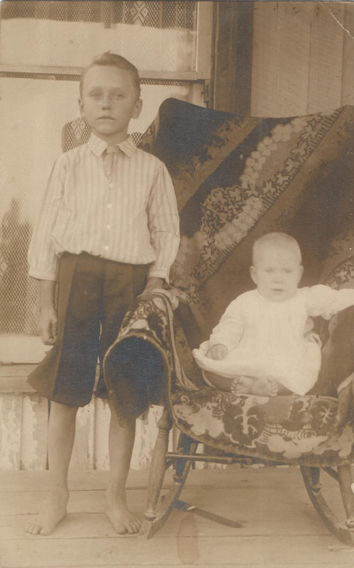 Young barefoot boy standing next to seated baby