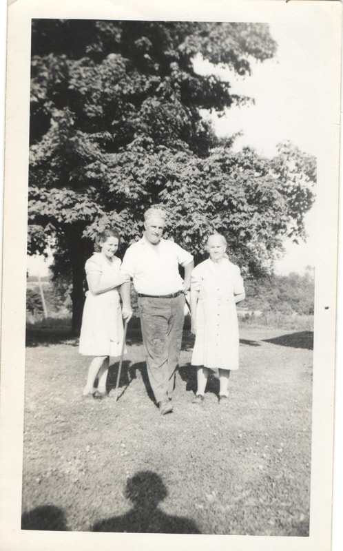 Man in cane standing with women in yard