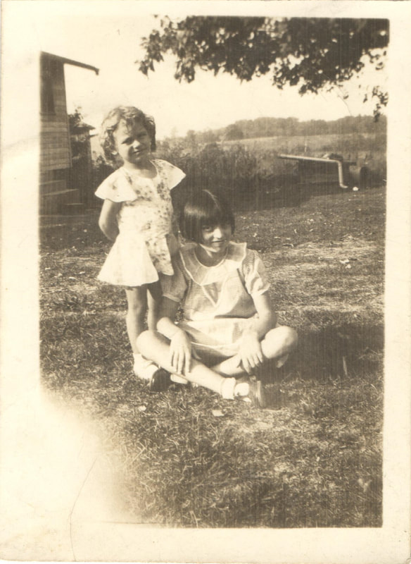 Young girl standing near seated girl in yard