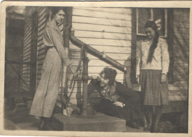 Women gathered around water pump in front of house