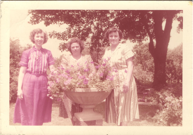 Women in dresses standing behind container of flowers