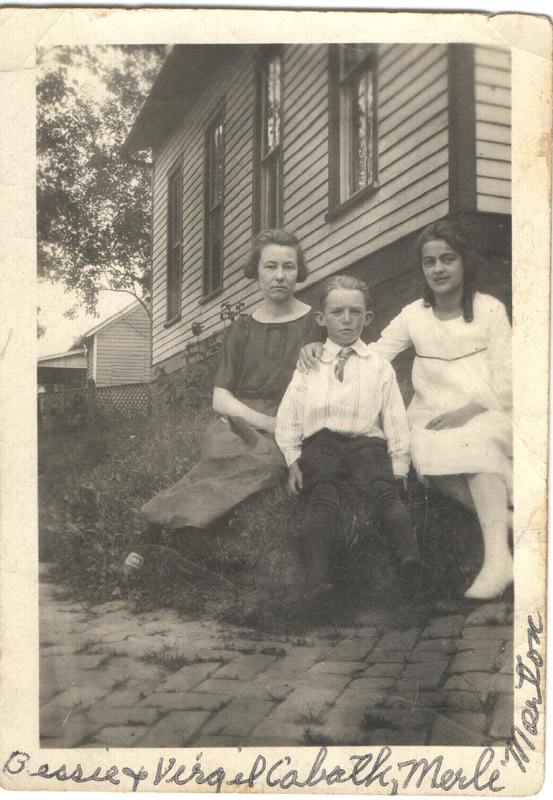 Women and young man seated in front of house
