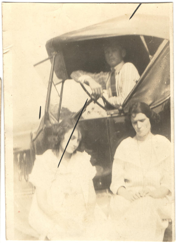 Man seated in car with women seated in front of car