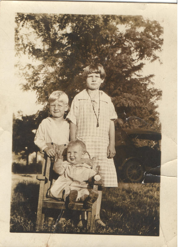 Young boy and girl standing behind baby seated in chair