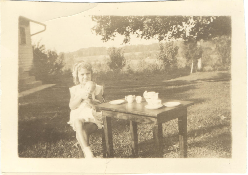 Young girl holding baby doll seated at table with tea set