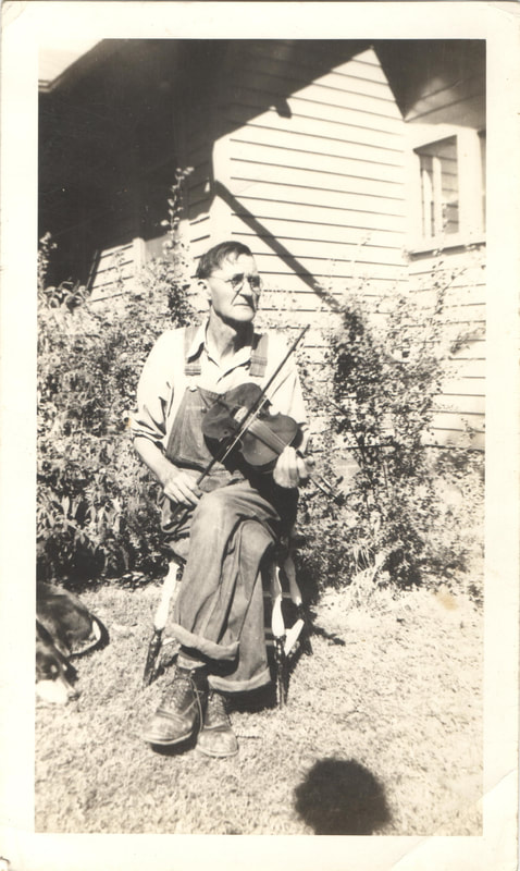 Elderly man in overalls seated with violin