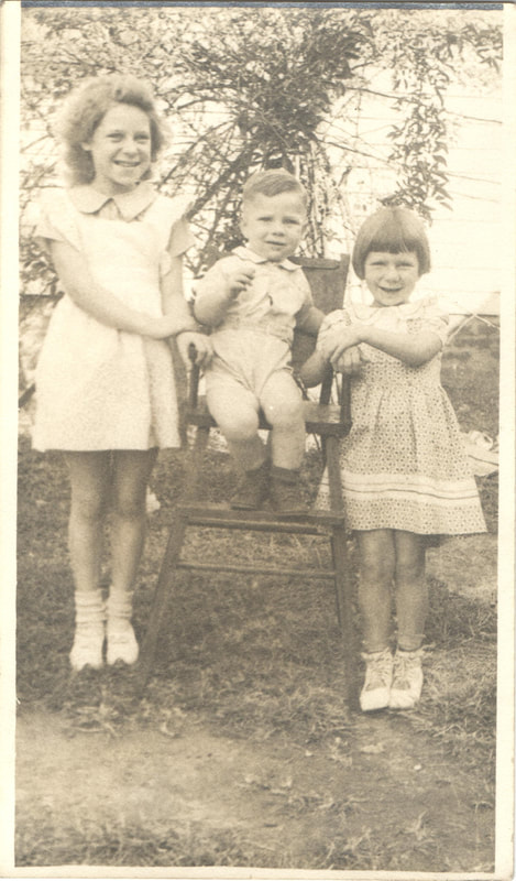 Young girls standing next to seated baby boy