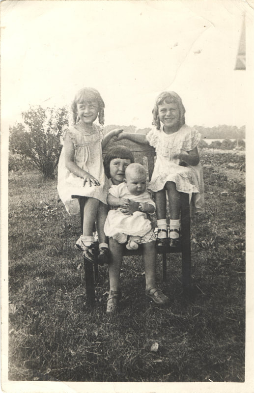 Young girls seated next to young girl holding baby