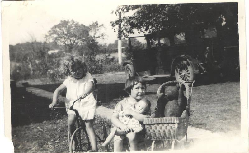 Young girl on tricycle next to young girl seated with doll