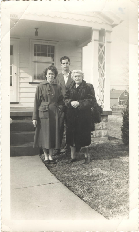Women in coats standing in front of man in front of house