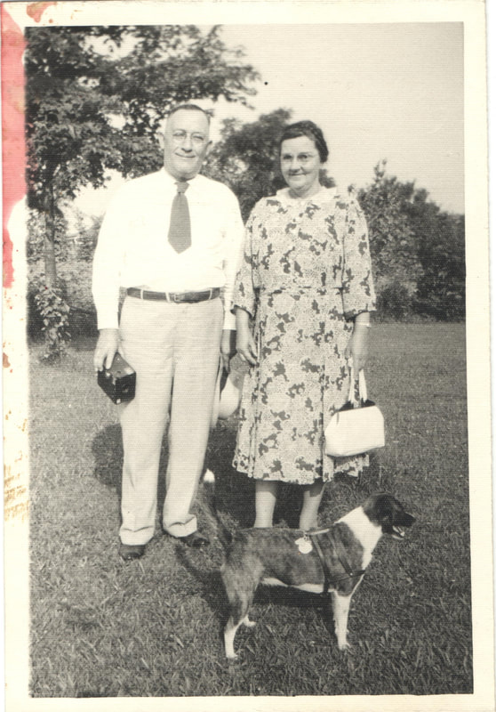 Elderly man and woman in dress clothes standing behind dog