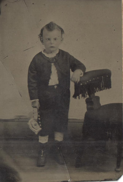 Young boy standing next to chair holding purse