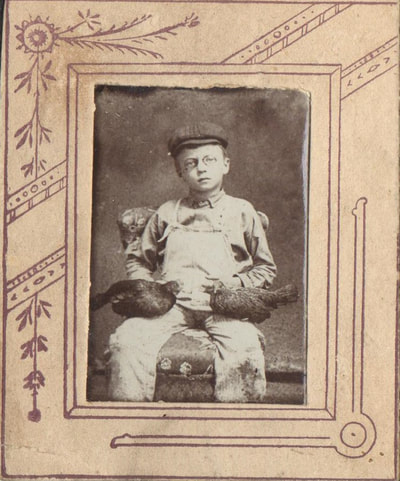 Young boy with glasses and hat seated with chickens