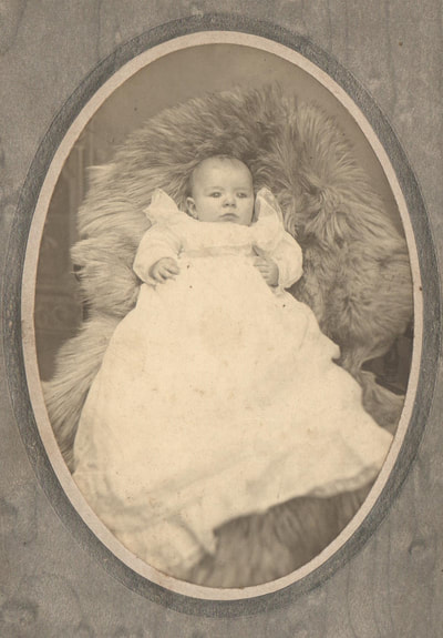 Baby in gown lying in fur rug