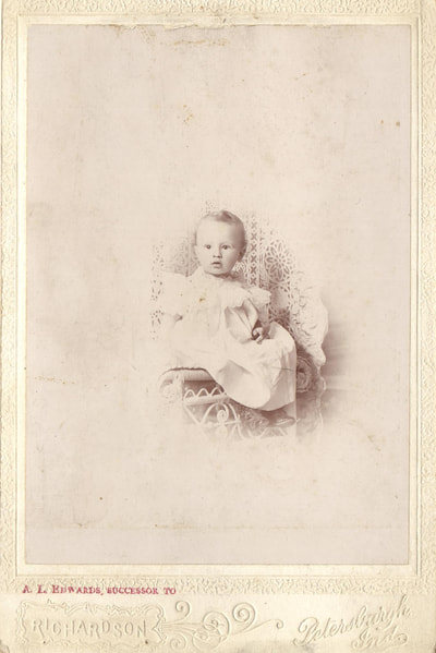 Baby in gown seated on chair