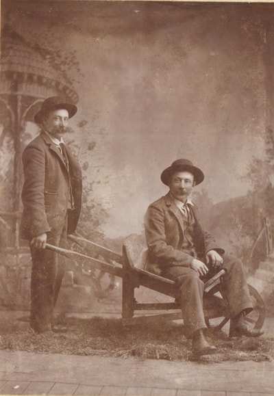 Men with mustaches and hats posed at wheelbarrow