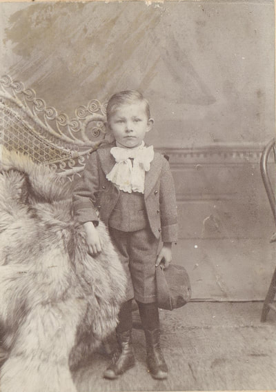  Young boy in fancy clothes standing next to chair with fur