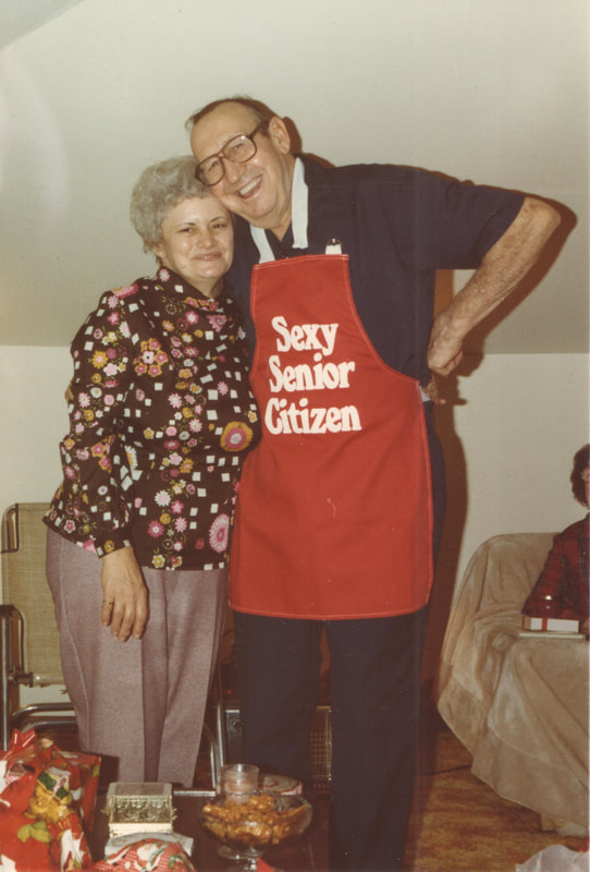 Elderly man poses with apron Christmas present and woman
